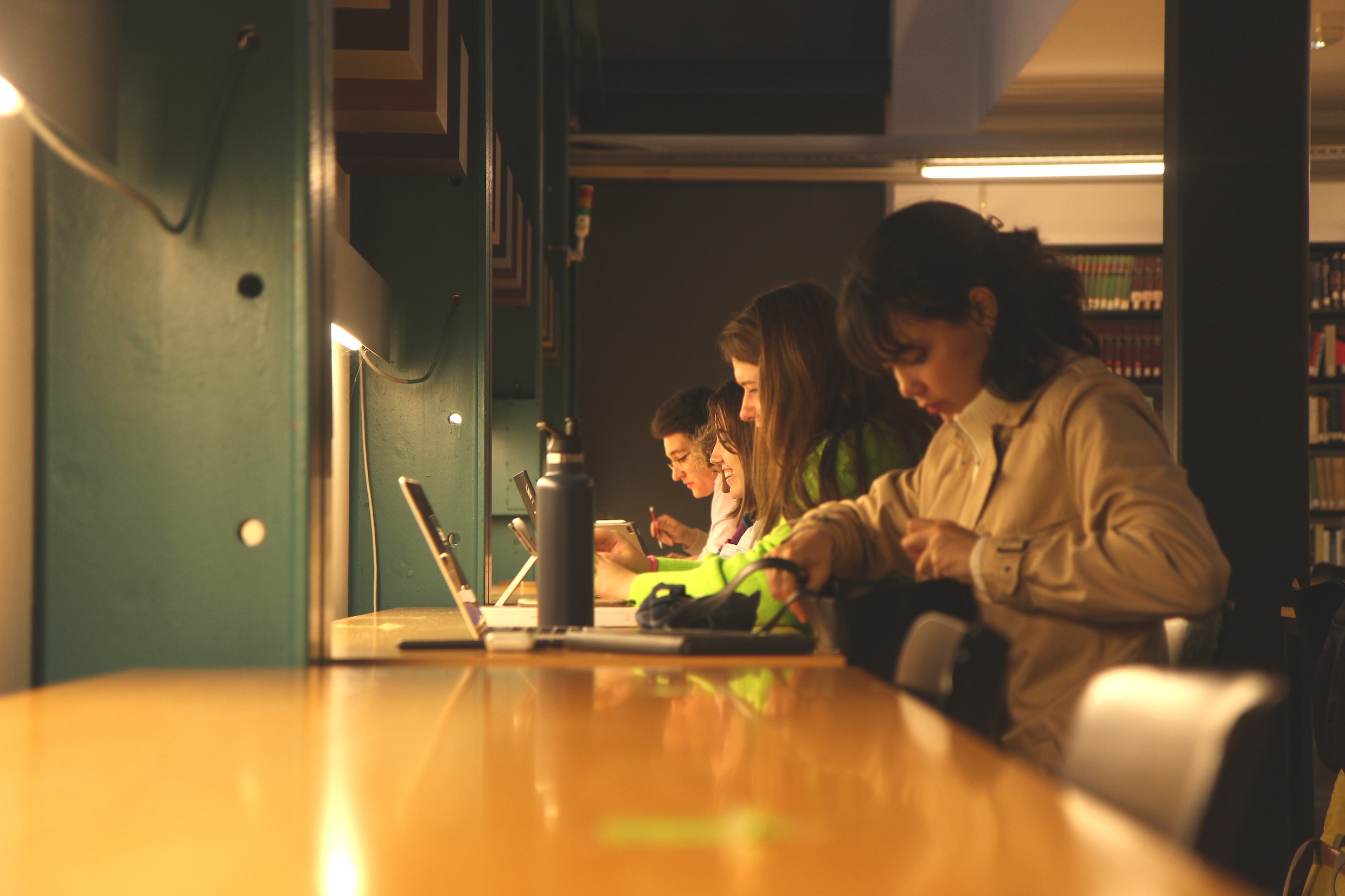 Das Bild zeigt Studierende, die an einem langen Tisch in der Bibliothek am Deutschen Seminar arbeiten. Ganz vorne holt eine Studentin grade etwas aus ihrer Tasche heraus.